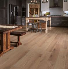 a large kitchen with wooden floors and dark colored cabinets, an island table and two stools