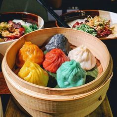 a wooden bowl filled with different colored dumplings on top of a table next to other bowls