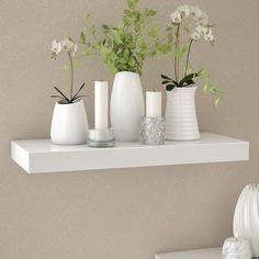 three white vases with flowers and greenery are on a shelf in the corner