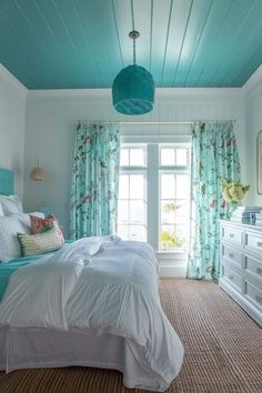 a bed room with a neatly made bed next to a window and a blue ceiling