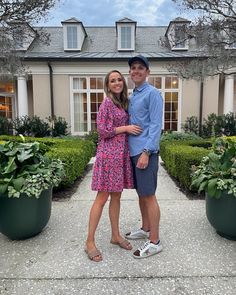 a man and woman standing next to each other in front of a house with potted plants