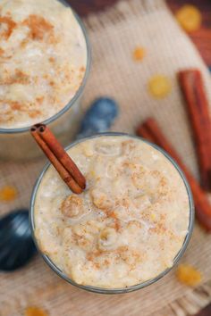 two glasses filled with food on top of a wooden table next to spoons and cinnamon sticks