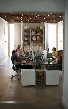 people sitting at desks in an office with computers on the tables and bookshelves