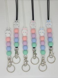 six keychains with different colored beads and bunny ears on each one, hanging from black cord