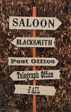 a pole with several signs on it in front of some bushes and trees, one sign is pointing to the right