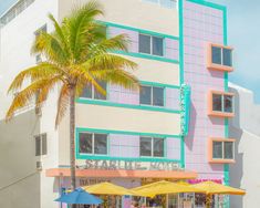 people are sitting under umbrellas in front of a building with a pink and blue facade