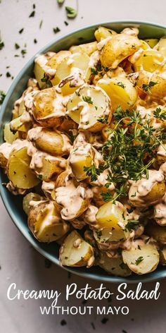 potato salad with creamy dressing in a blue bowl on a white tablecloth next to sliced green herbs