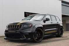 a black jeep with gold stripes parked in front of a white garage door and building