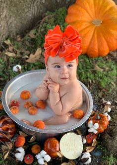 a baby sitting in a metal bowl with oranges on the ground