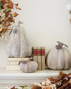 three white pumpkins sitting on top of a mantle next to some books and flowers