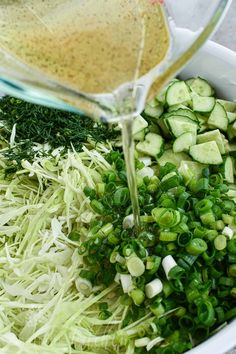 someone is pouring dressing into a bowl filled with shredded green onions and cucumbers