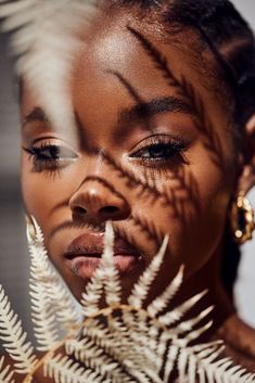 a close up of a woman's face with leaves in front of her