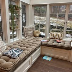 a sun room with lots of windows and pillows on the bench in front of it