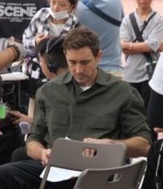 a man sitting in a chair using a laptop computer while surrounded by people standing around him