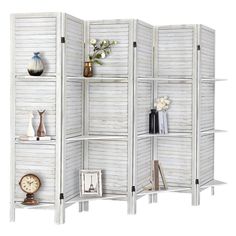 a room divider made out of white shutters with shelves and vases on each side