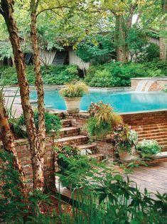 an outdoor swimming pool surrounded by greenery and trees with steps leading up to it