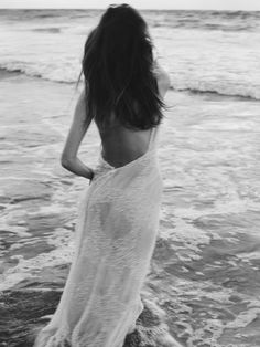 a woman is standing in the water at the beach and looking out into the ocean