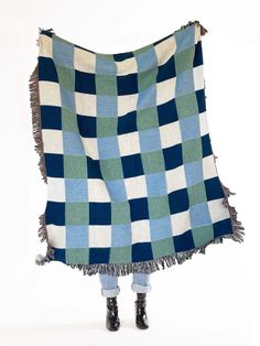 a woman is standing under a blue and green checkered blanket with fringes on it