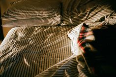 an unmade bed with striped sheets and pillows