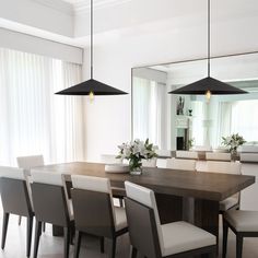 a dining room table with chairs and lights hanging from it's ceiling, in front of a large mirror