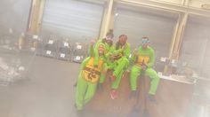 four people dressed in green and yellow sitting on top of a luggage cart at an airport