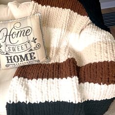 a white and brown blanket sitting on top of a bed next to a pillow that says home sweet home