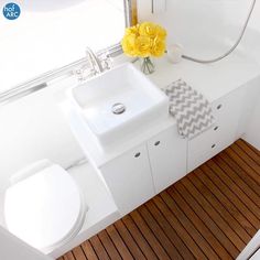 a white sink sitting next to a toilet on top of a wooden floored bathroom