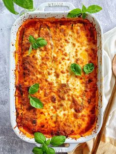 a casserole dish with cheese and spinach leaves on the side next to a spoon