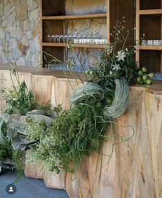 an arrangement of greenery is placed on a wooden shelf in front of a stone wall