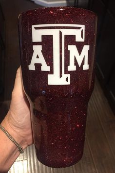 a person holding up a red tumbler with the word texas on it