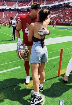 a man and woman hug on the field at a football game