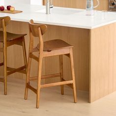 two wooden stools sit in front of an island counter with apples on the counter