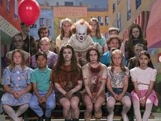 a group of people sitting on top of a bench in front of a clown mask