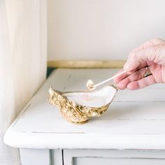 a person is holding a spoon over a bowl with gold leaf decoration on the side