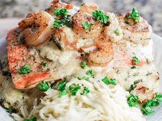 a white plate topped with pasta and shrimp covered in sauce, garnished with parsley