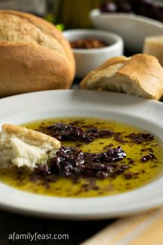 a white plate topped with soup next to bread and other foods on a table top