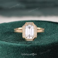 an emerald colored diamond ring sitting on top of a green velvet box