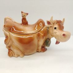 a ceramic cow figurine sitting on top of a white table next to a small dog