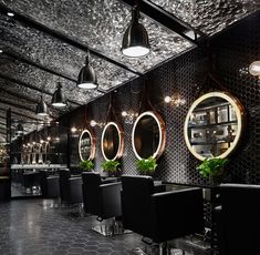 the interior of a salon with black chairs and round mirrors on the wall, along with potted plants