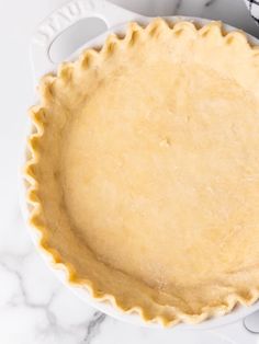 an uncooked pie crust in a white dish on a marble counter top with utensils