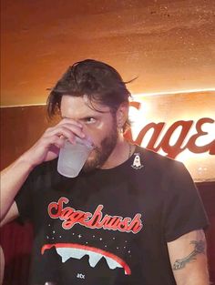 a man drinking from a plastic cup in front of a neon sign