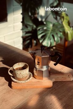 a wooden table topped with a cup and saucer next to a potted plant