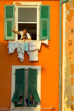 two people are hanging out the window and drying their clothes in front of an orange building