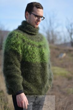 a man with glasses wearing a green sweater and black pants standing in front of a field