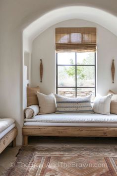 a bed sitting under a window in a bedroom next to a wooden bench with pillows on it