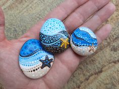 three painted rocks in the palm of someone's hand with starfishs and seashells on them