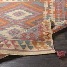 a multicolored rug with tassels and fringe on the bottom, laying on a wooden floor