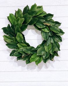 a green wreath is hanging on a white wooden wall with wood planks in the background