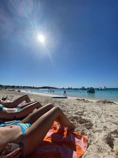 two people laying on the beach with boats in the water and sun shining over them