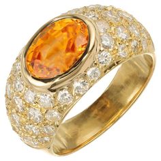 a ring with an orange stone surrounded by white and yellow diamonds in gold plating